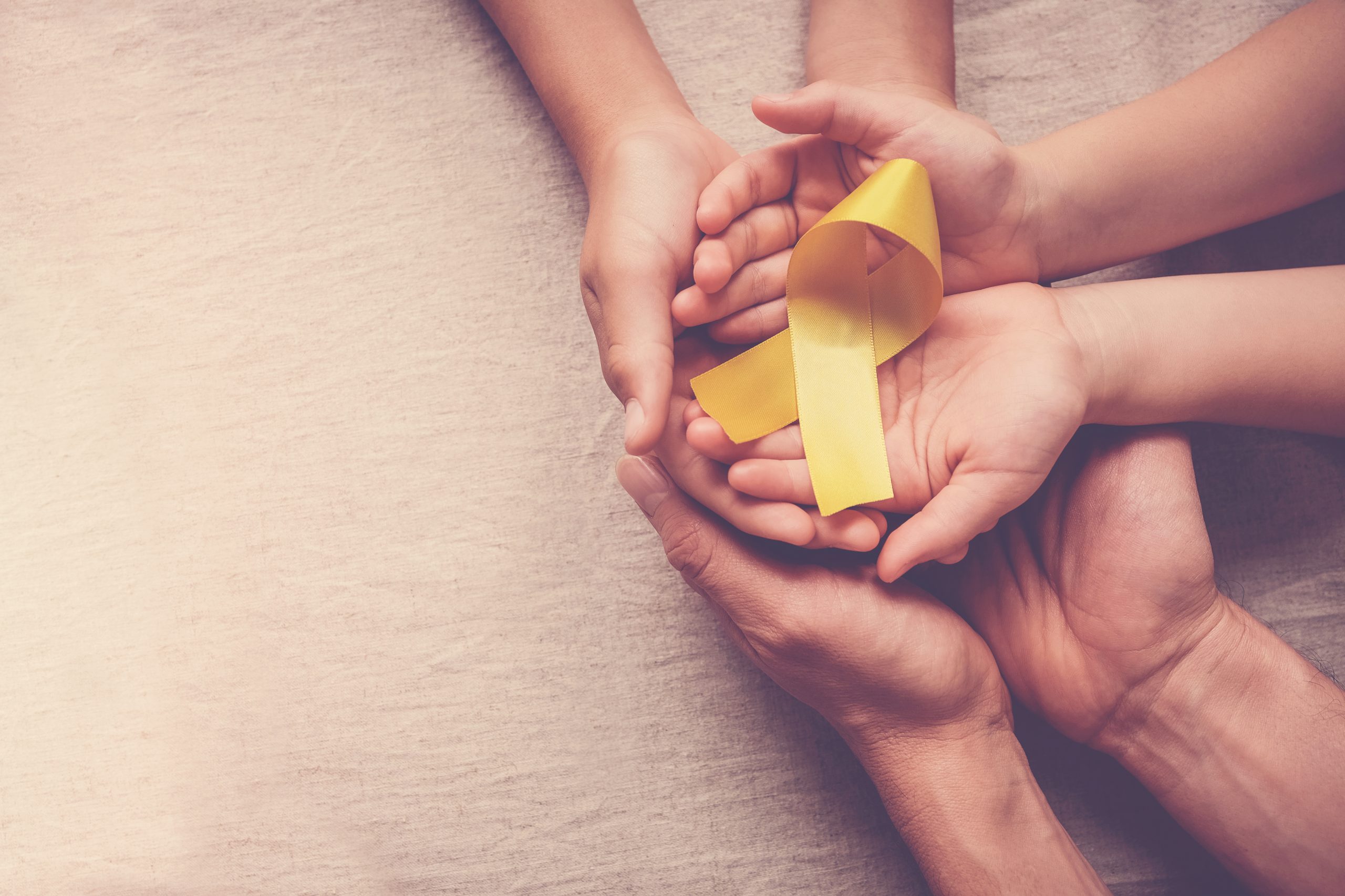 Adult,And,Children,Hands,Holding,Yellow,Gold,Ribbon,,Sarcoma,Awareness,